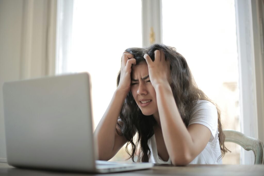 Estrés emocional Mujer joven frente a una laptop mostrando signos de estrés emocional y ansiedad mientras se sostiene la cabeza con ambas manos.